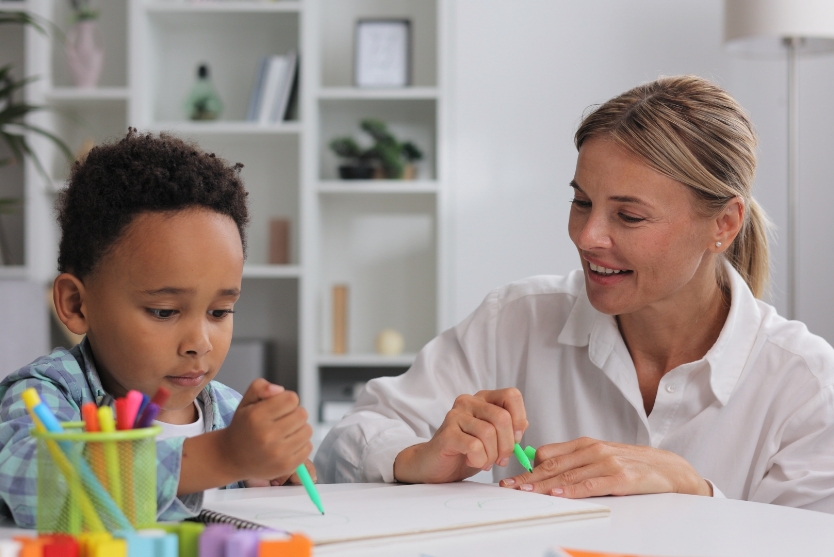 A teacher or caretaker draws with a school-age child at a table.